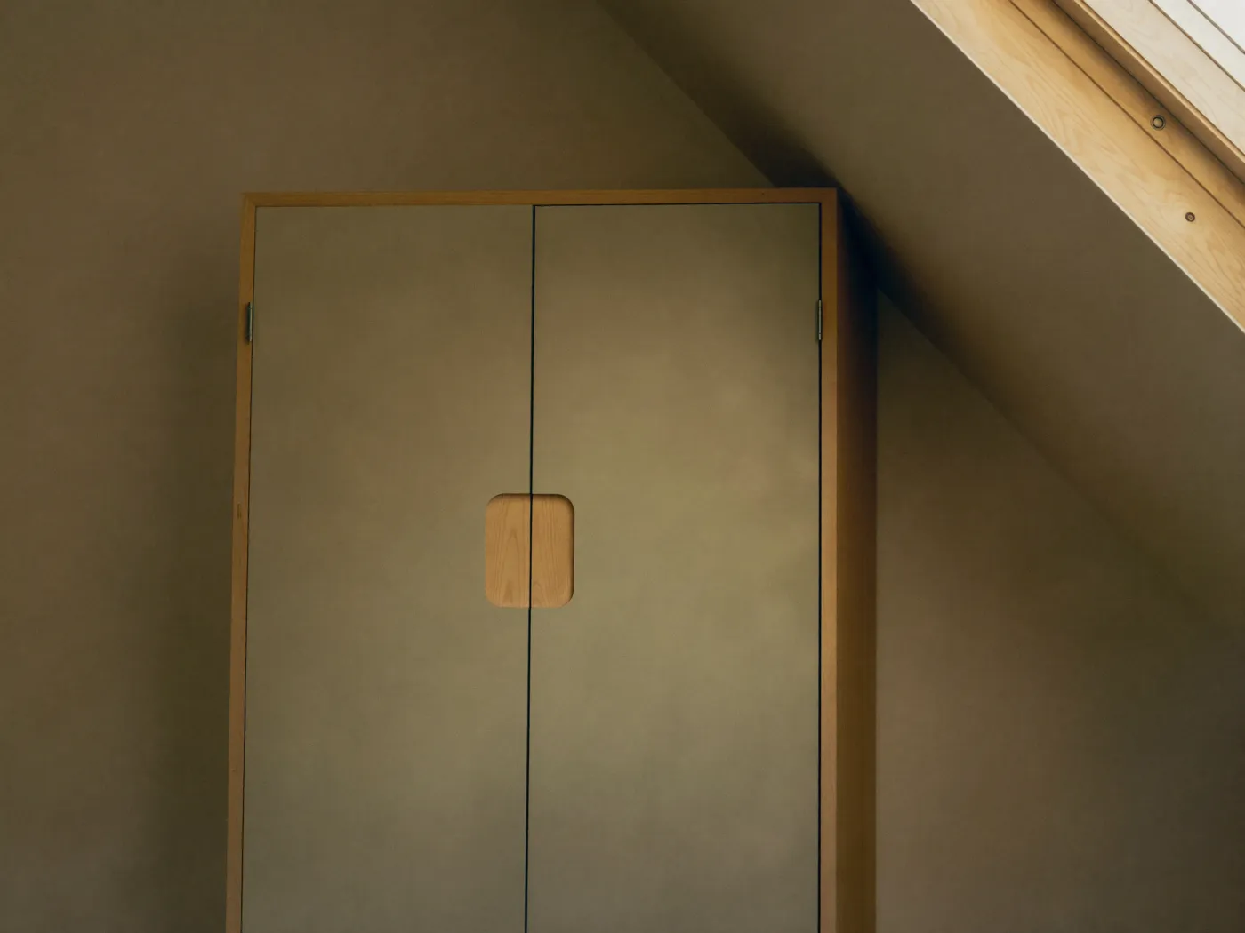 Dressing encastré sous un rampant de toit, portes pleines et poignée en bois