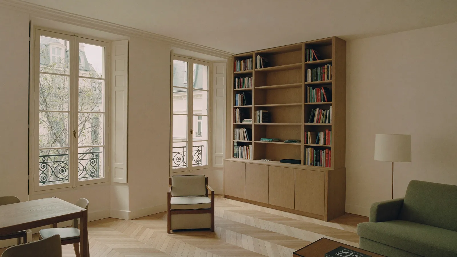 Salon parisien avec une bibliothèque en chêne massif intégrée sur toute la hauteur du mur, parquet à chevrons et hautes fenêtres