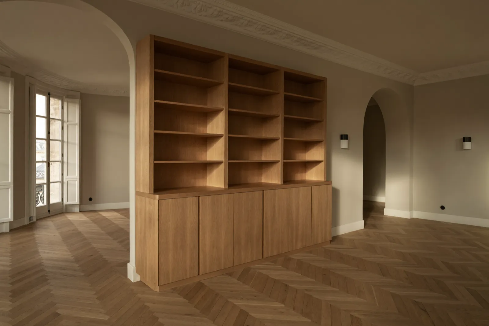 Bibliothèque en chêne naturel du sol au plafond avec rangements intégrés dans un appartement parisien classique