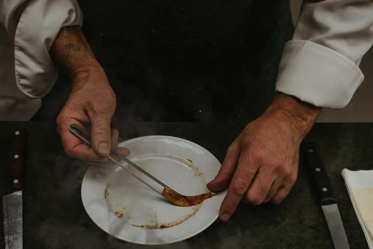 Mains d'un cuisinier terminant une assiette à la pince, vues de dessus