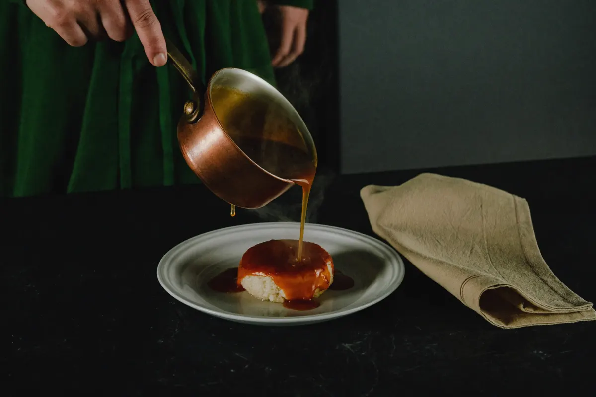 Mains versant une sauce ambrée depuis une casserole en cuivre