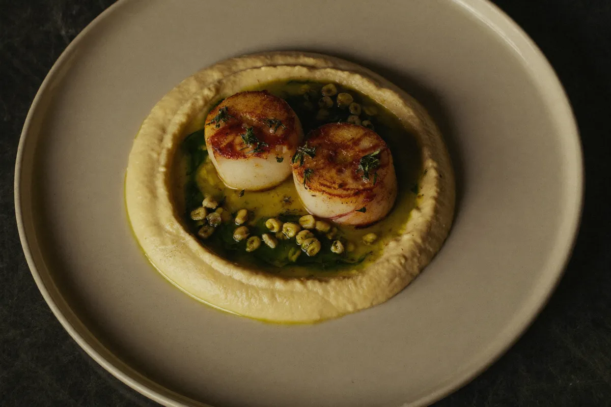 Saint-Jacques snackées, purée de chou-fleur et sarrasin torréfié sur une assiette en céramique crème